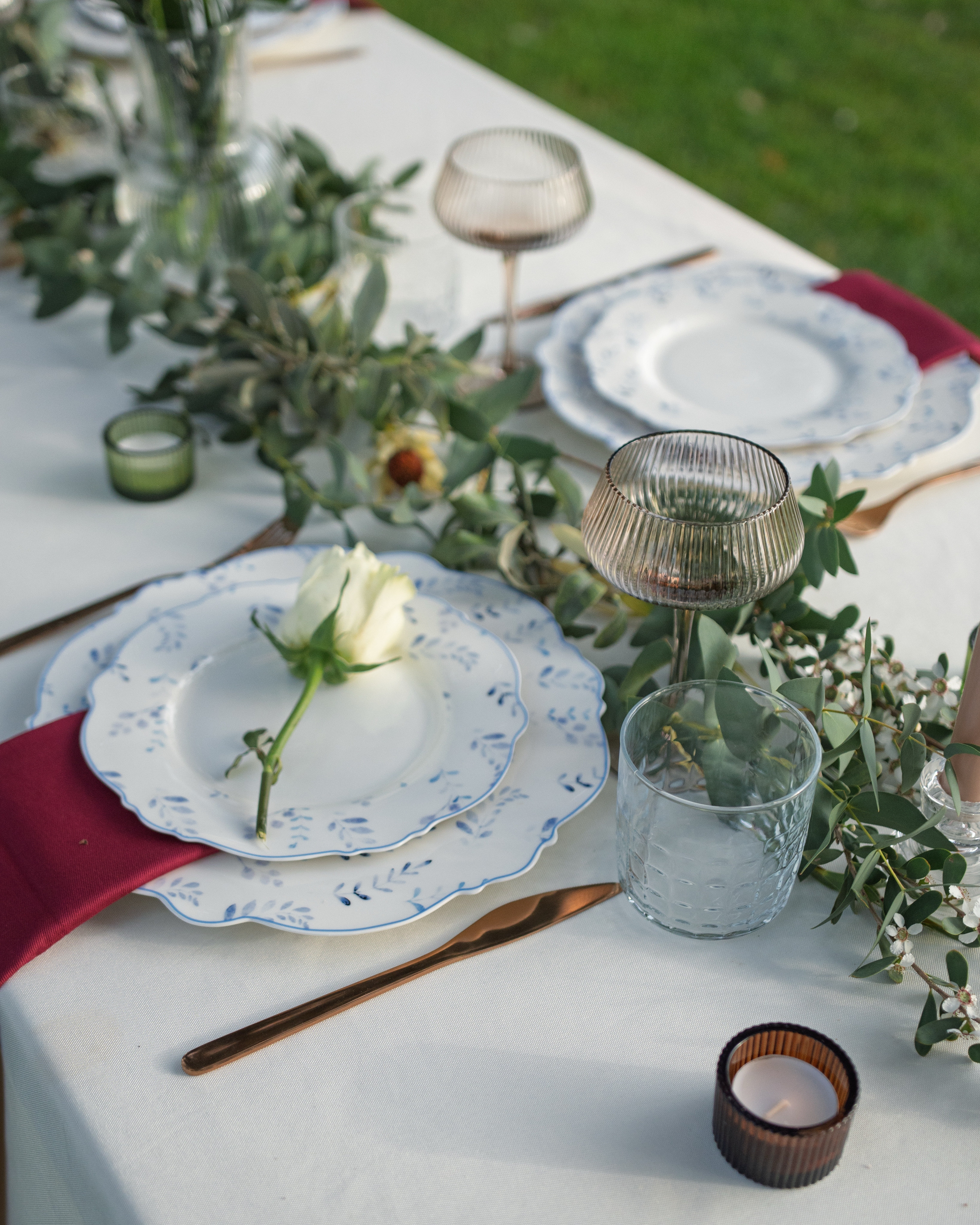 Elegant outdoor wedding tablescape with eucalyptus garland, blue and white china, and burgundy linen — designed by KarolinaBLevents